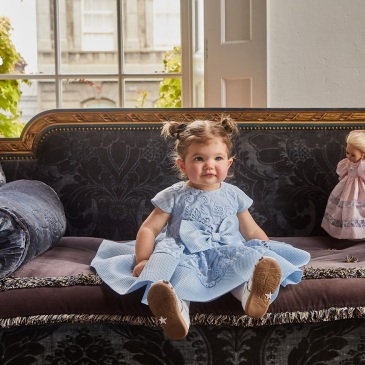 baby girl sitting on a couch with a blue designer dress